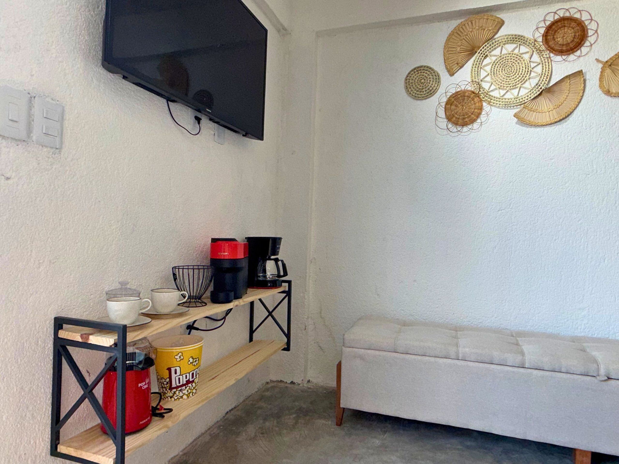 A room with a TV mounted on the wall, a shelf with kitchen items, a white sofa, and decorative wall art.