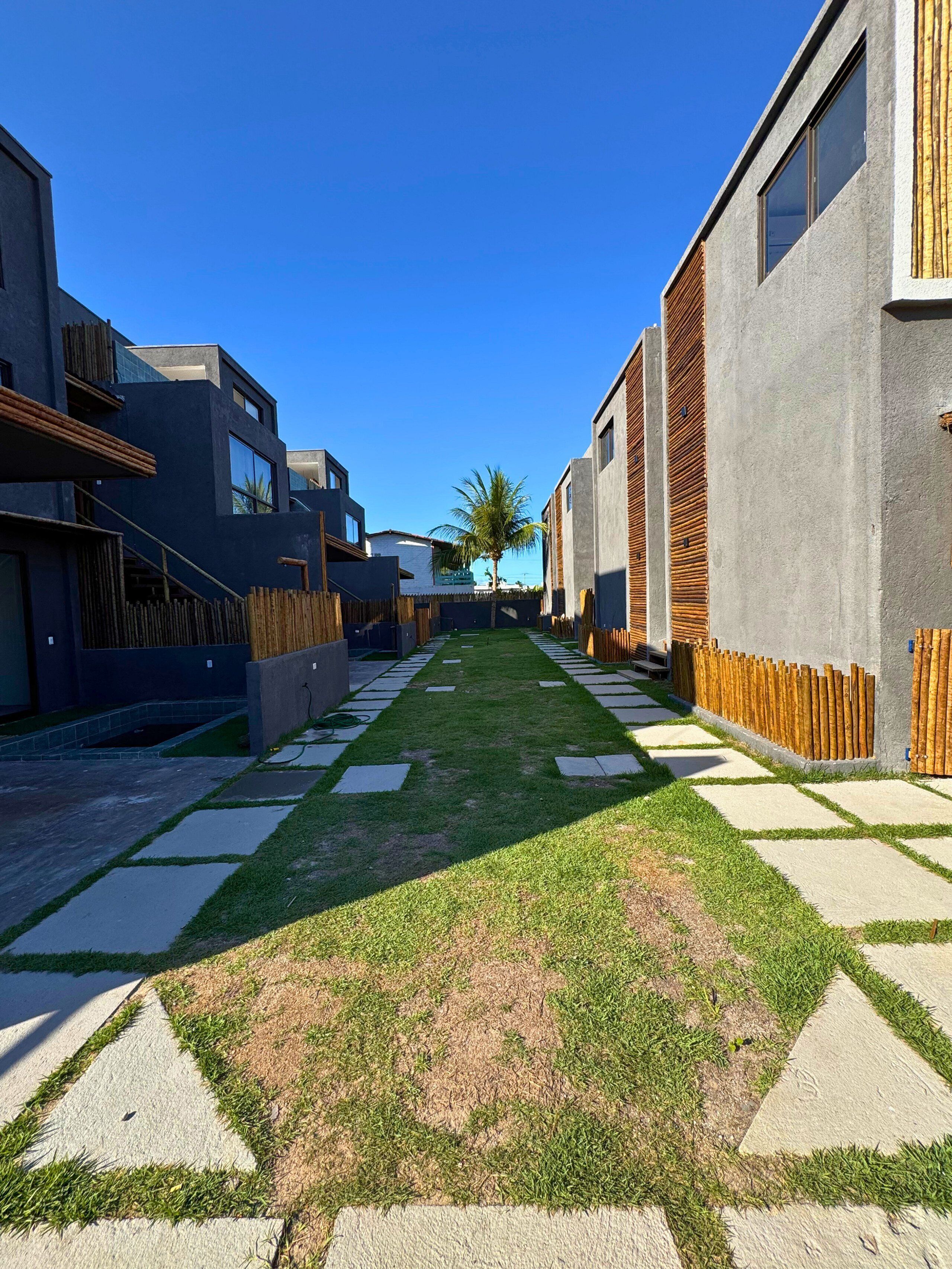 Un área residencial moderna con un camino central, casas con grandes ventanales y una palmera al fondo.