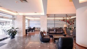 Un vestíbulo moderno con área de descanso, una mesa de recepción y un amplio ventanal.