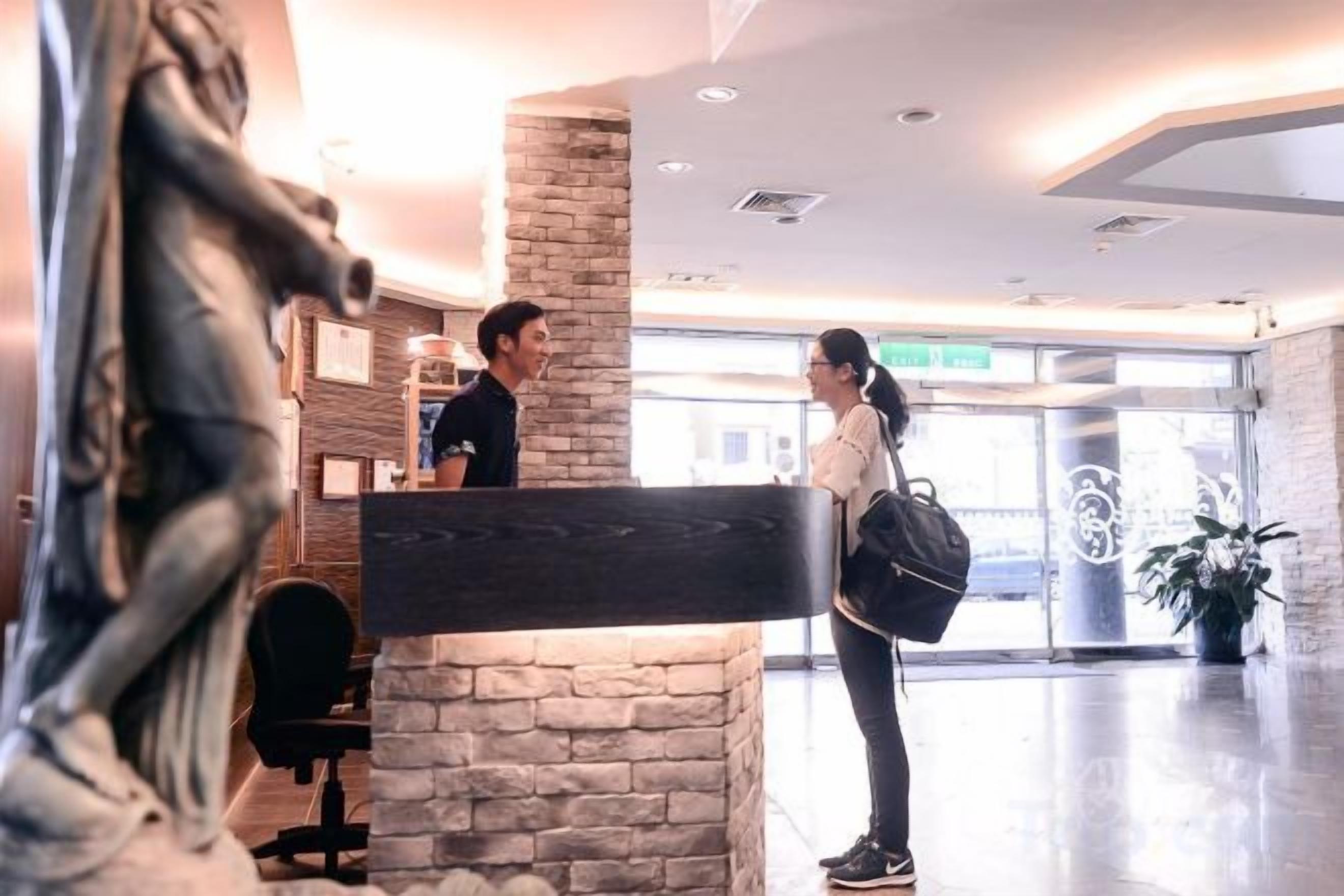 A reception area with a receptionist, a guest, and a statue.