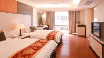 A hotel room with two beds, a TV, a desk, and a view of the outdoors.