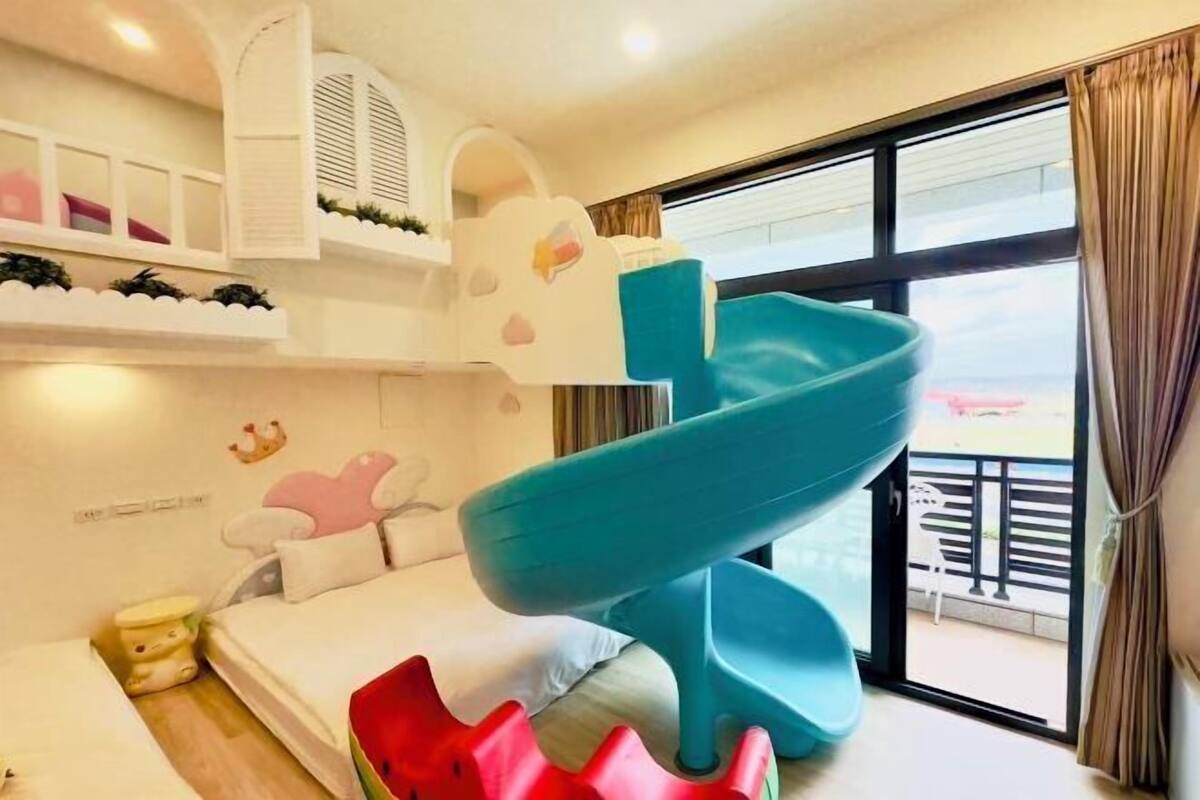 A children's room with a slide, bunk beds, and a window with a view.