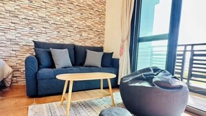 A modern living room with a stone wall, a blue sofa, a wooden coffee table, and a bean bag chair. - Sun Shine Bed and Breakfast (Pingtung)