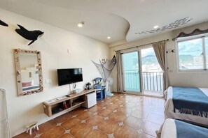 A hotel room with a TV, a bed, a balcony with a view, and a tiled floor. - Sun Shine Bed and Breakfast (Pingtung)