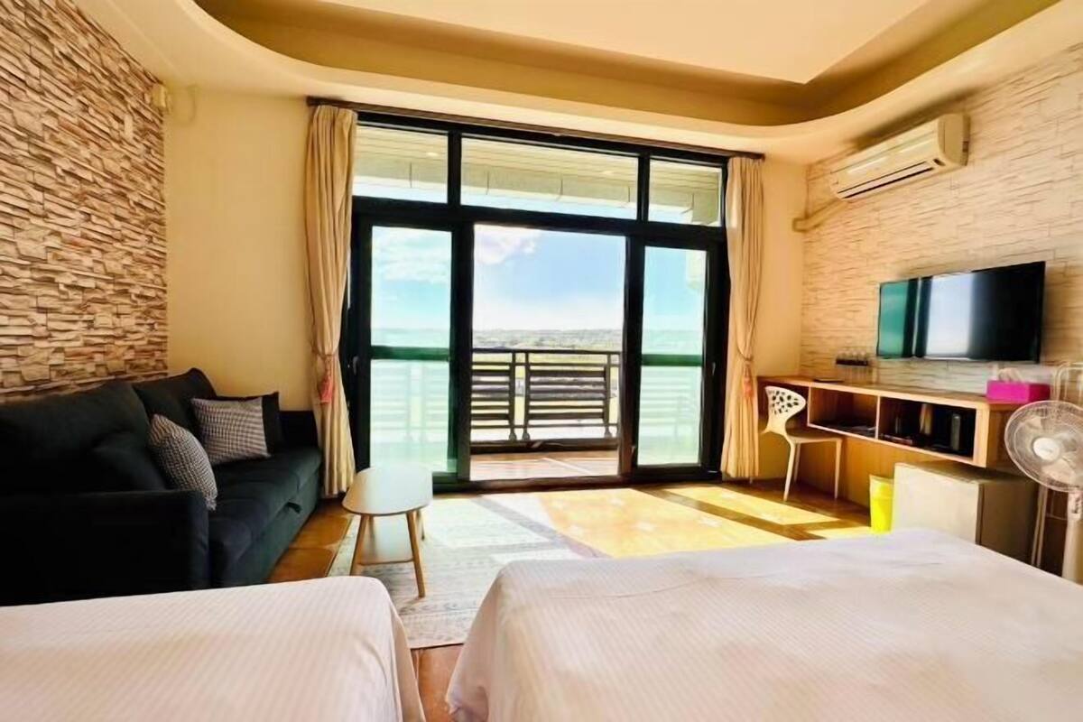 A hotel room with a large sliding glass door to a balcony, a bed, a desk, a chair, and a television.