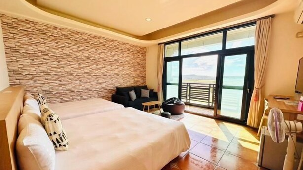 A hotel room with a large bed, a stone wall, a balcony with a view, and a fan. - Sun Shine Bed and Breakfast (Pingtung)