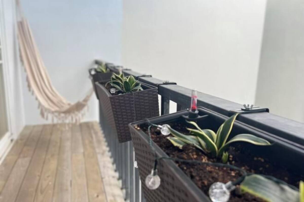 A balcony with potted plants, a hammock, and a wooden floor.