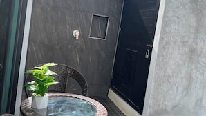 Un petit espace extérieur clos, comprenant une table en verre et une chaise, un pot de fleurs, une douche et une porte.