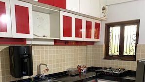A kitchen with red and white cabinets, a black countertop, a water dispenser, and a window with decorative iron bars. - Casa Nadella (Alto de Porvorim)