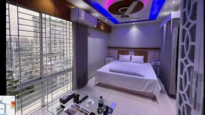A modern hotel room with a large bed, a ceiling fan, and a view of the city through floor-to-ceiling windows. - Hotel The Manha LTD Purana Paltan (Dhaka)