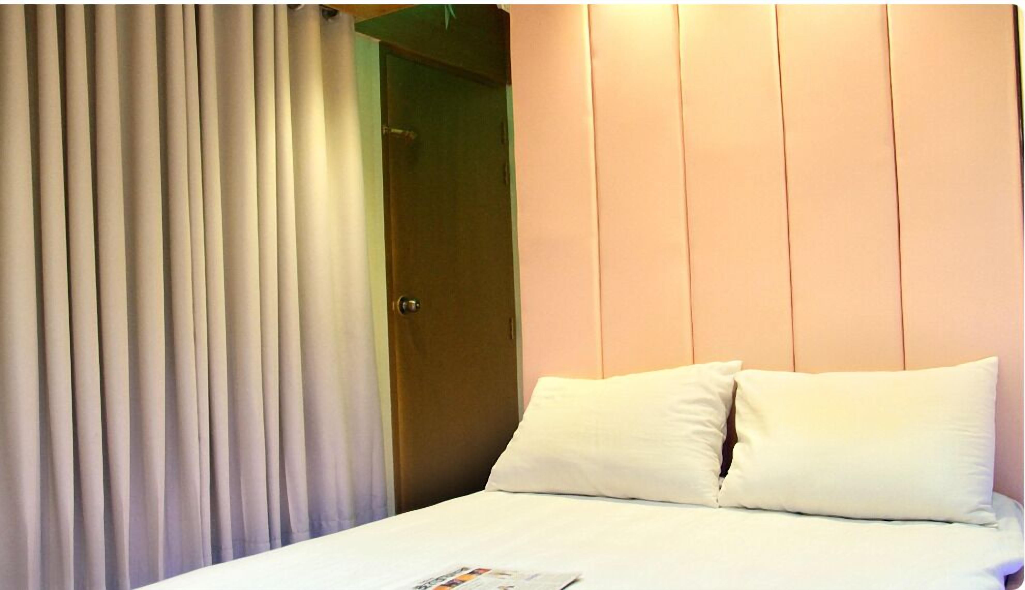 Una habitación de hotel con cama, ropa de cama blanca, una puerta y una cortina.