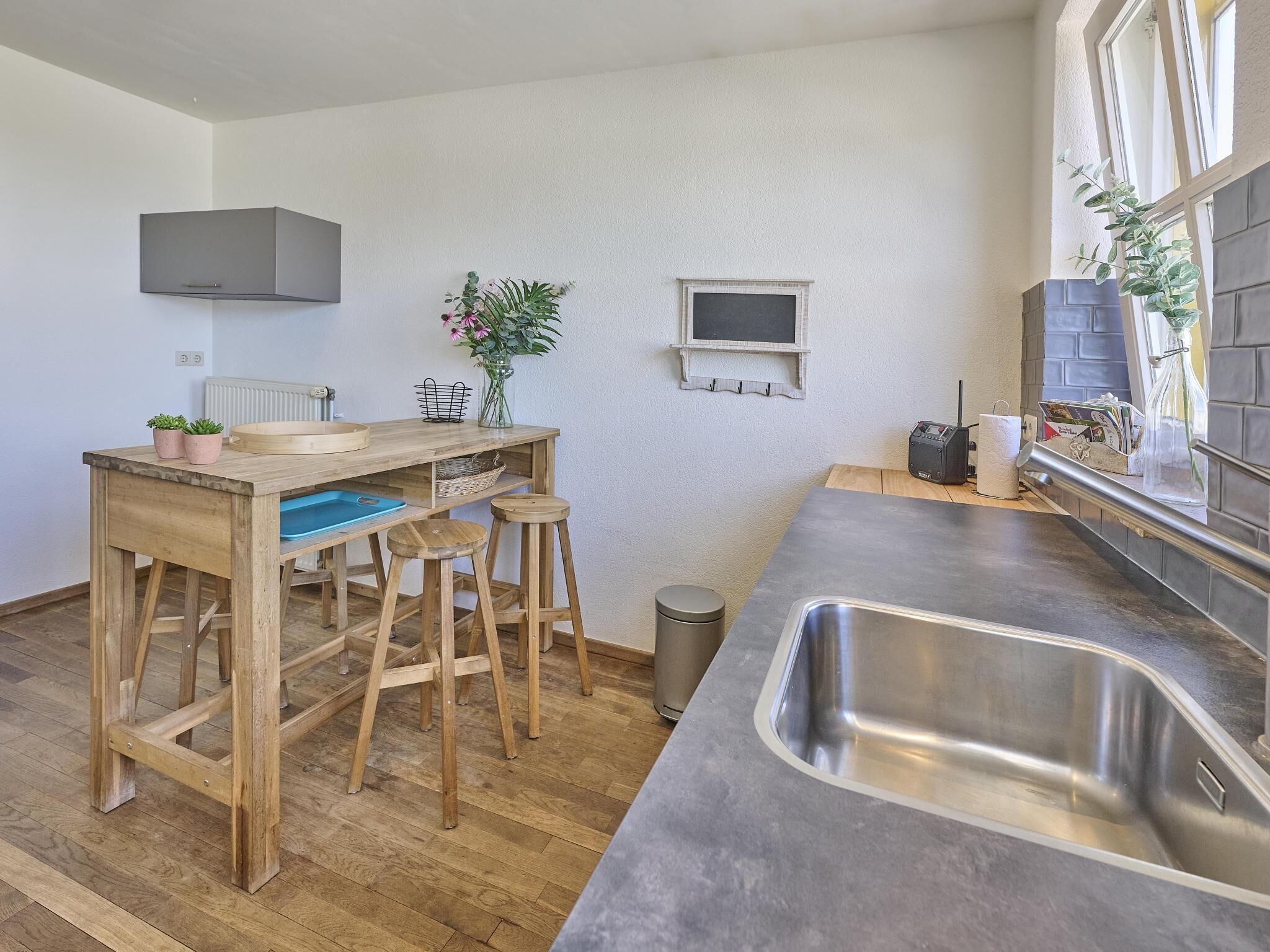 Una cocina moderna con un taburete de madera, un lavamanos de acero inoxidable y una ventana pequeña.