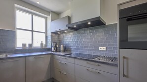 A modern kitchen with grey cabinets, a black range hood, and a window with natural light. - Group farmhouse with large garden and wideviews (Elsendorp)