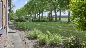 A garden with a brick building, a pathway, and a grassy area with trees. - Group farmhouse with large garden and wideviews (Elsendorp)