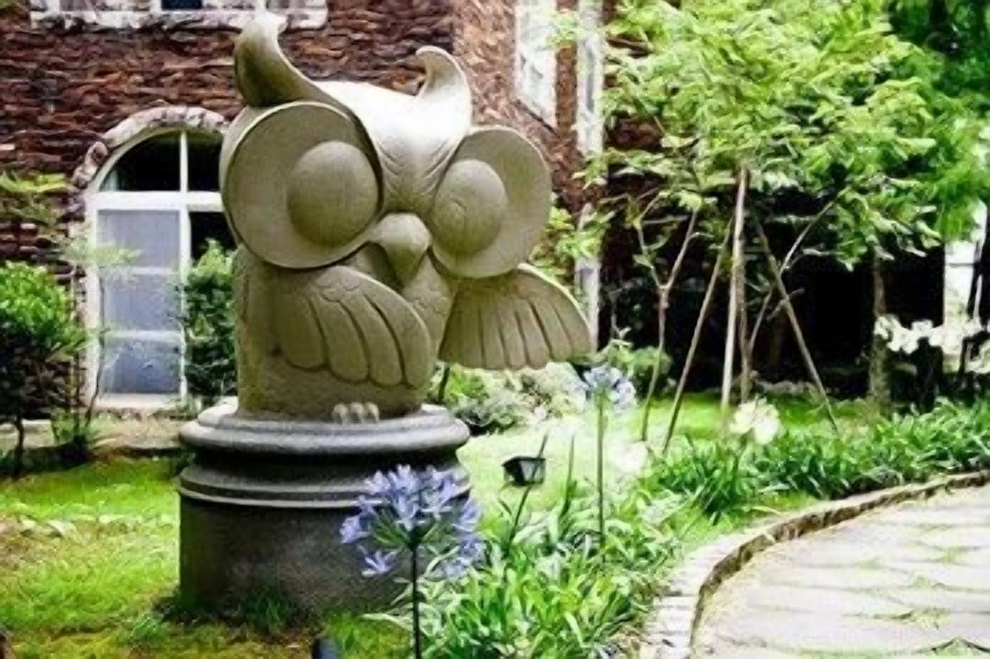 A garden with a stone owl sculpture, a brick building, and a pathway.