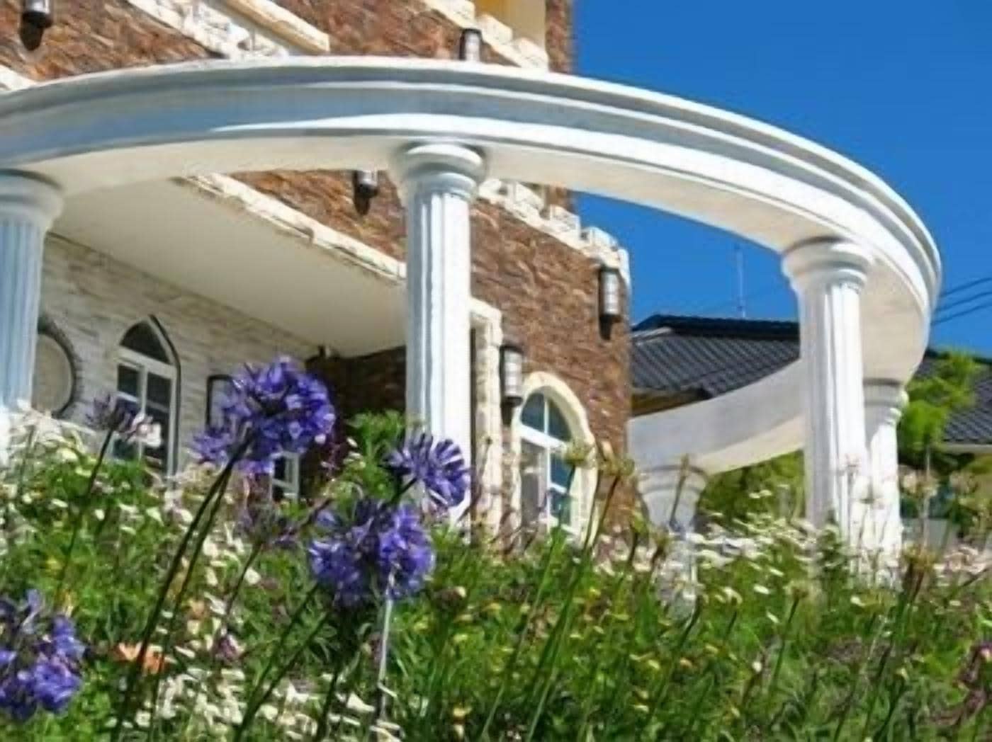 A building with a white porch supported by columns, surrounded by flowers.