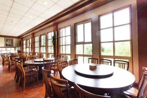 A spacious dining area with multiple round tables and chairs, large windows allowing natural light, and a tiled floor. - Liching Garden Village (Nantou)