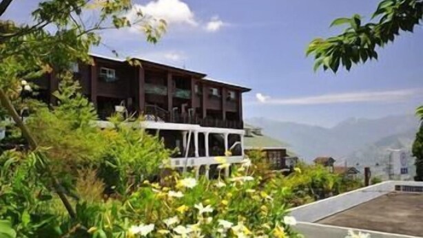 A multi-story building with balconies, surrounded by lush greenery and mountains in the background. - Liching Garden Village (Nantou)