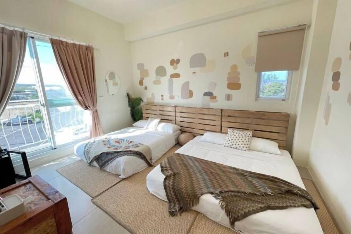 A hotel room with two beds, a large window with curtains, a wooden headboard, and a wall with abstract art.