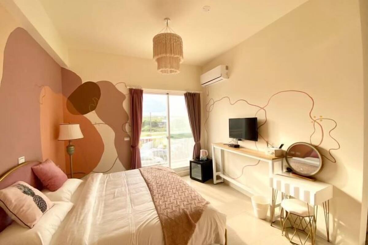 A bedroom with a bed, a desk, a TV, and a balcony.