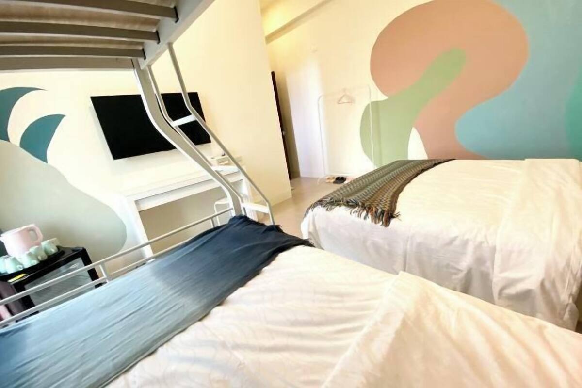 A hotel room with a bunk bed, a bedside table with a lamp, and a wall with abstract art.