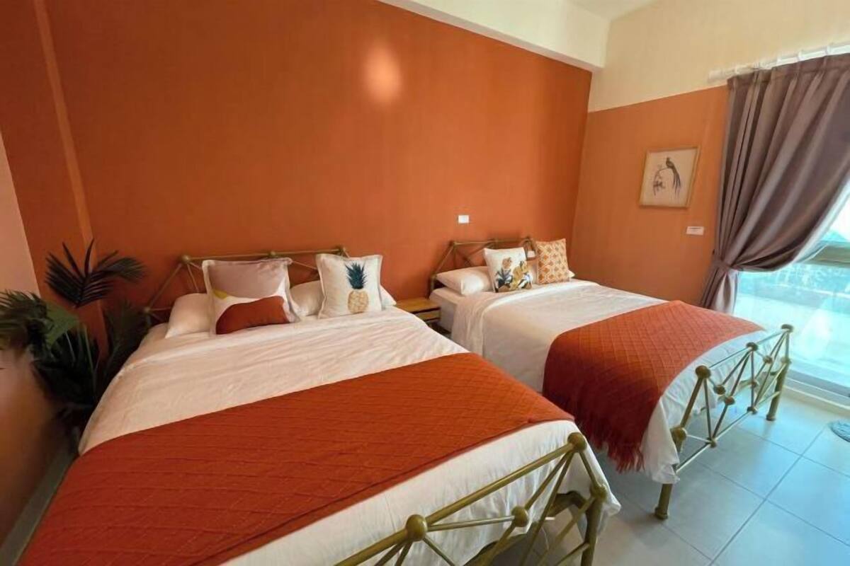 A hotel room with two beds, each with a wooden frame and white bedding. The room has a large window with curtains and a view of the outdoors.