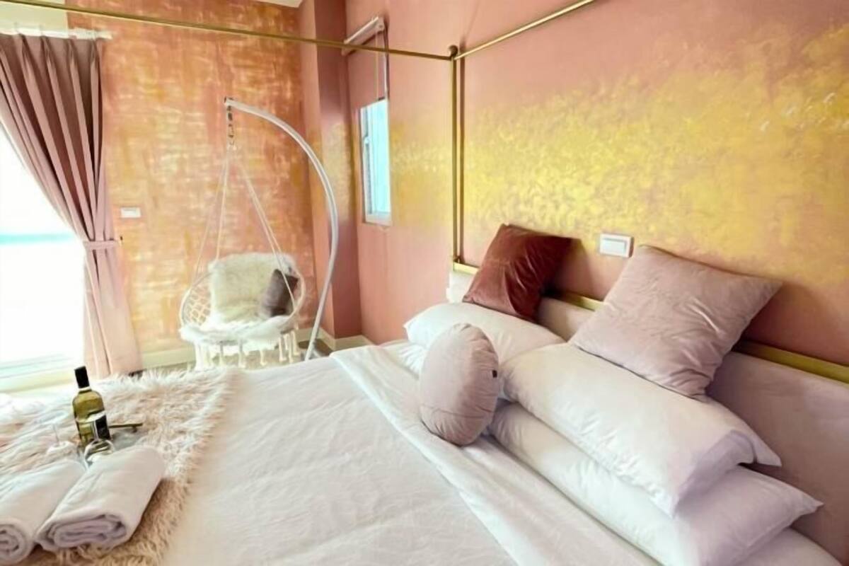 A bedroom with a bed, pillows, a hanging chair, and a bottle of lotion.