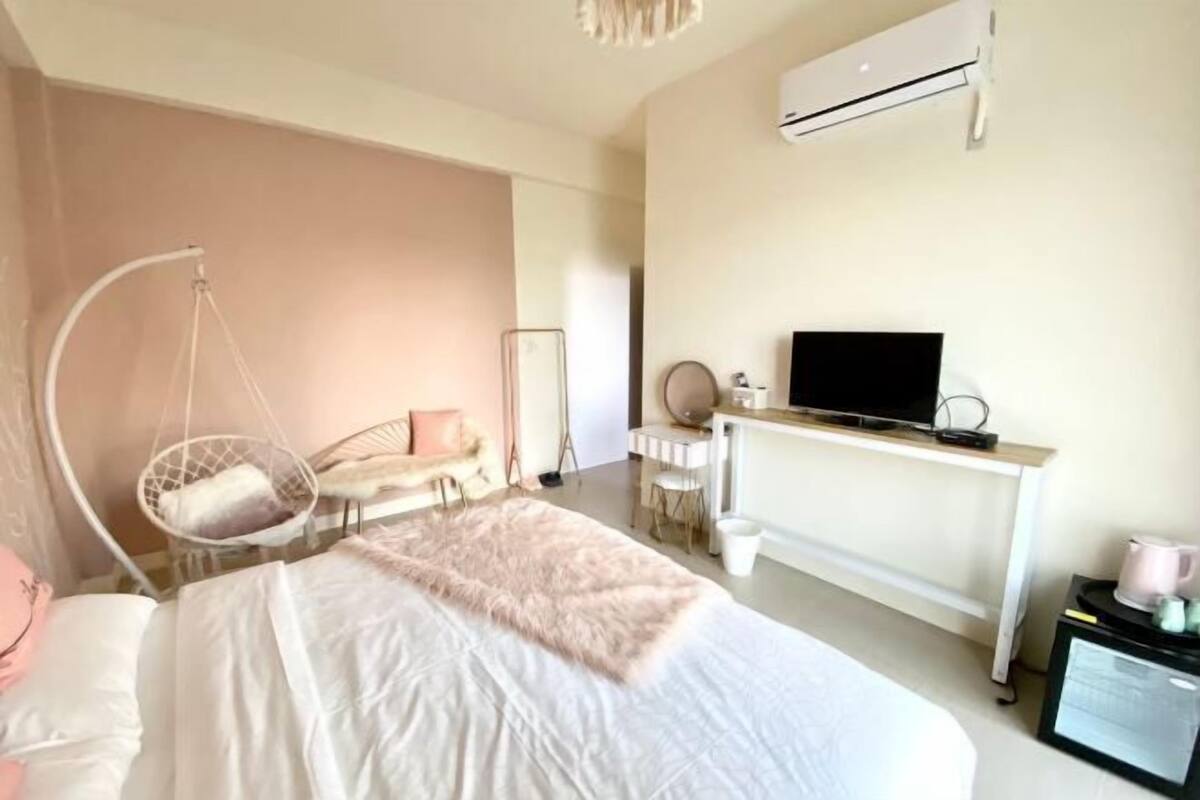 A modern hotel room with a bed, a hanging chair, a desk with a TV, and a white air conditioning unit.