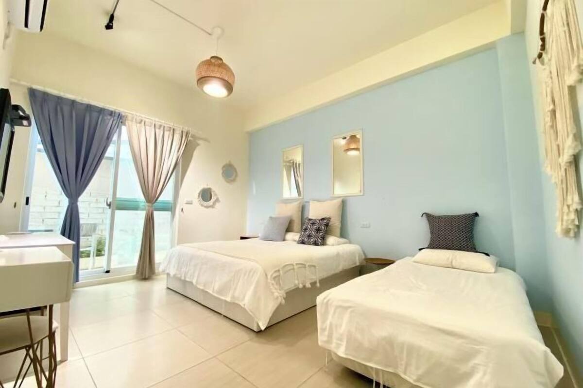 A room with two beds, a desk, and a large window with curtains.