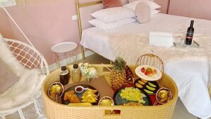 A neatly arranged bed with a white and gold headboard, a wicker basket with food and drinks, and a white chair with a fluffy cushion. - Pinky Promise Villa (Pingtung)