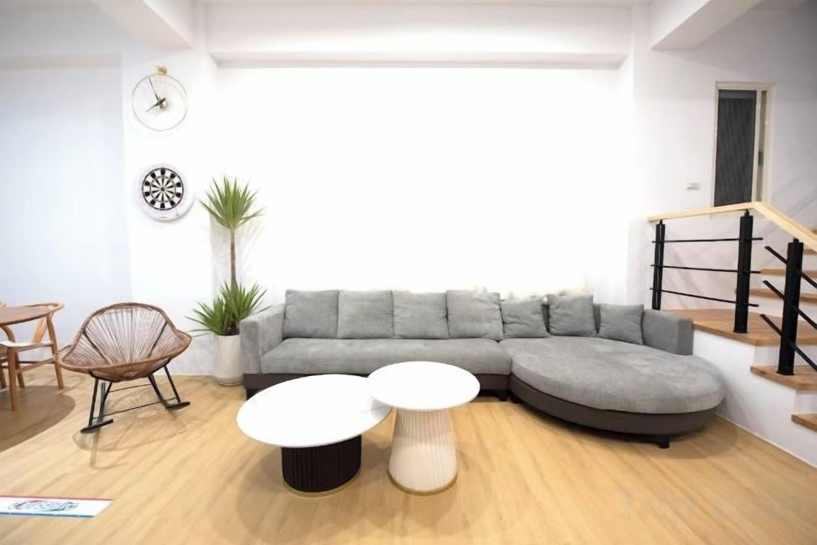 Una sala moderna con un sofá modular, dos mesas de centro, una planta en maceta y una escalera.