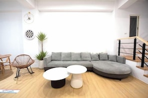 A modern living room with a sectional sofa, two coffee tables, a potted plant, and a staircase. - Sun eden (Nantou)