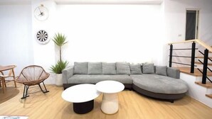 A modern living room with a grey sectional sofa, two round coffee tables, a wicker chair, a potted plant, and a staircase to the right. - Sun eden (Nantou)