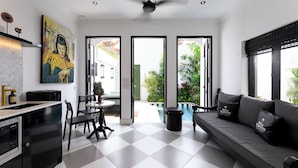 A modern kitchen with a black and white checkered floor, a dining area with a round table and chairs, and a living area with a sofa and a large window. - Villa Martini Beachside 5  (Canggu)