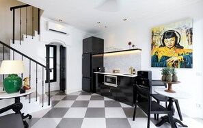 A modern kitchen with a checkered floor, a dining area with a table and chairs, a staircase with black railings, and a large painting on the wall. - Villa Martini Beachside 5  (Canggu)