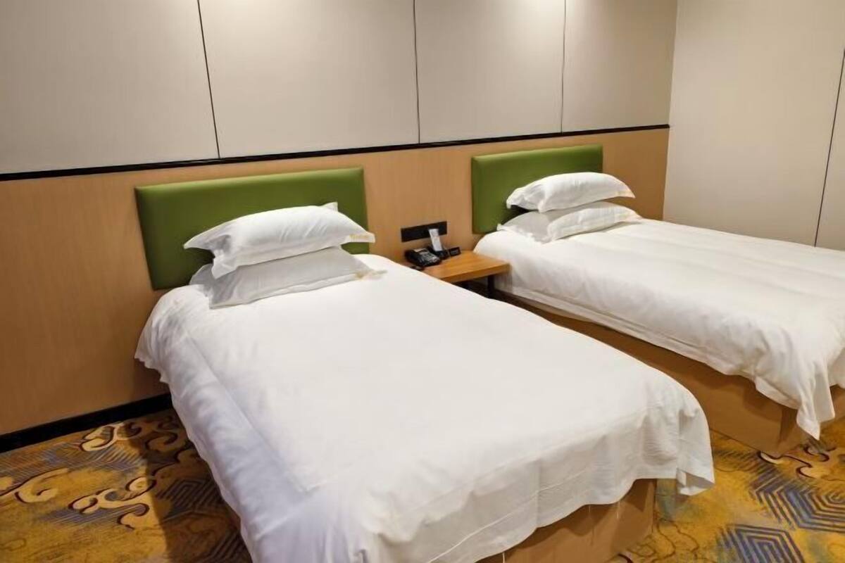 A hotel room with two single beds, a bedside table with a phone, and a patterned carpet.