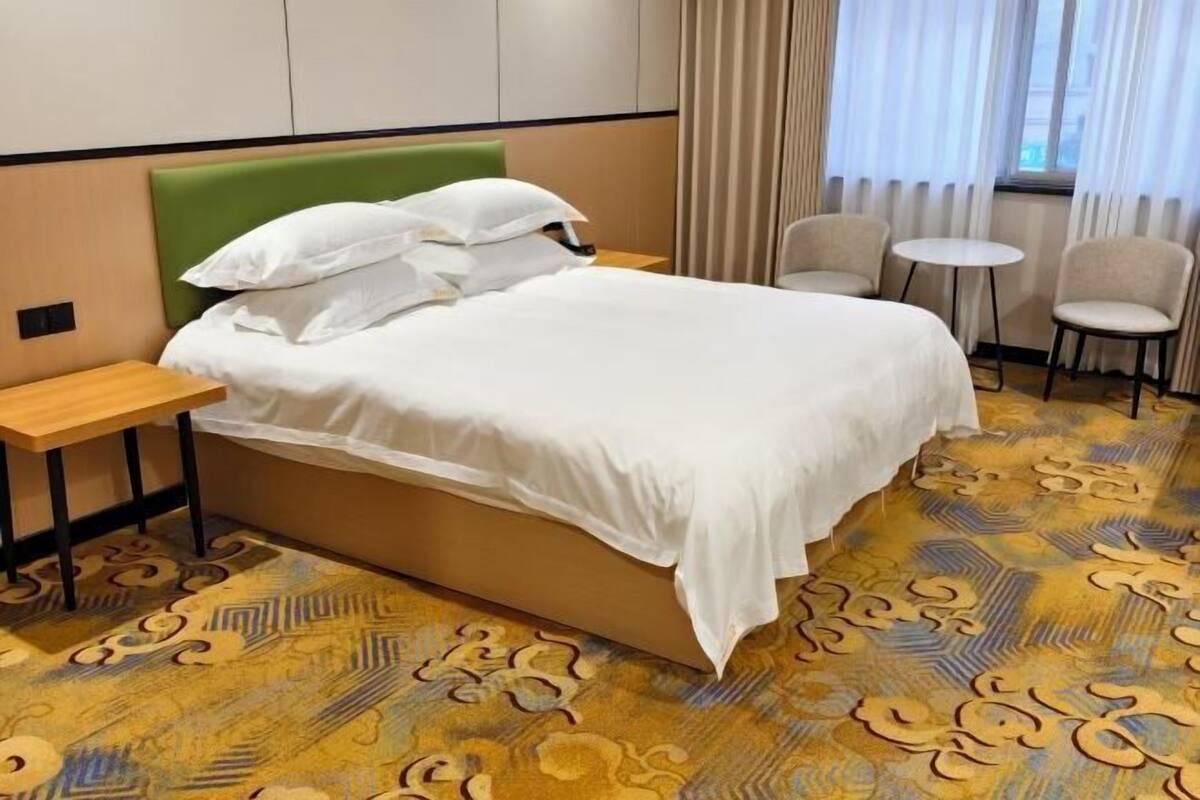 A hotel room with a bed, two chairs, a small table, and a patterned carpet.