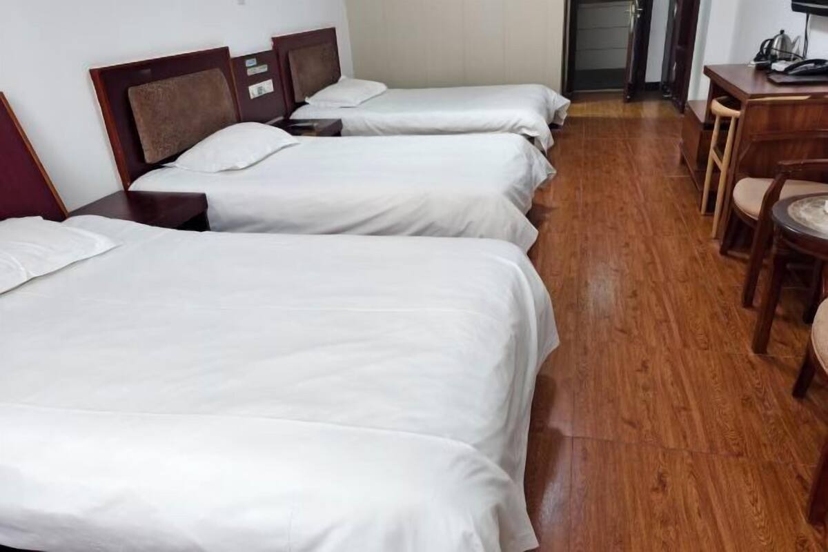 A hotel room with three beds, wooden flooring, a desk with a chair, and a television.