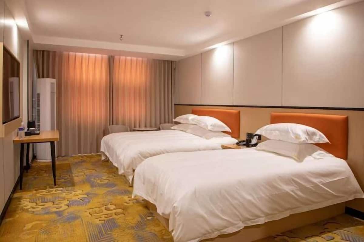 A hotel room with two beds, a desk, and a large window with curtains.