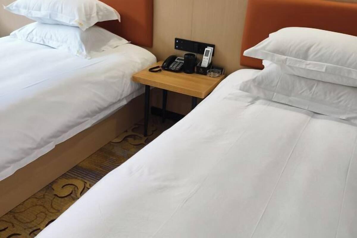 Two single beds with white linens, a wooden nightstand with a telephone, and a wall-mounted phone.