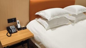 A hotel room with a bed, white pillows, a wooden nightstand with a phone, a glass of water, and a small box. - Hongshi Road Branch (Junan County)