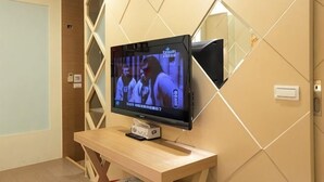 Uma televisão sobre uma escrivaninha de madeira em um quarto com design geométrico na parede.