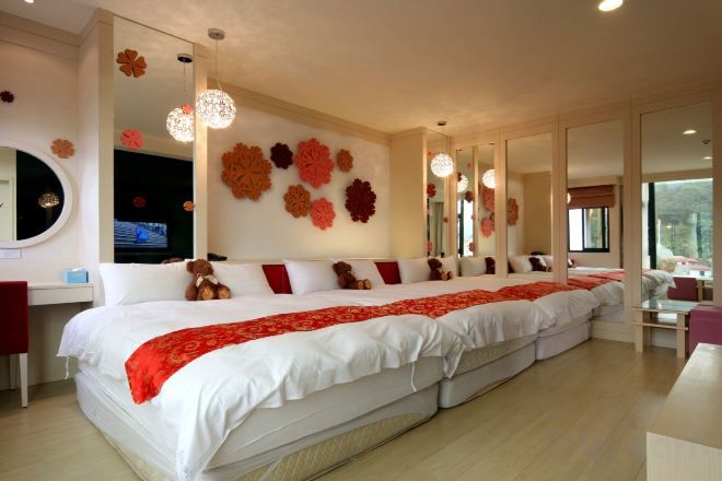 A large bed with a red and white bedspread, a television on a stand, and a wall with large flower decorations.