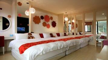 A large bed with a red and white bedspread, a television on a stand, and a wall with large flower decorations.