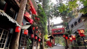 A narrow street with traditional architecture, red lanterns, and a red bridge. - The M Village (Nantou)