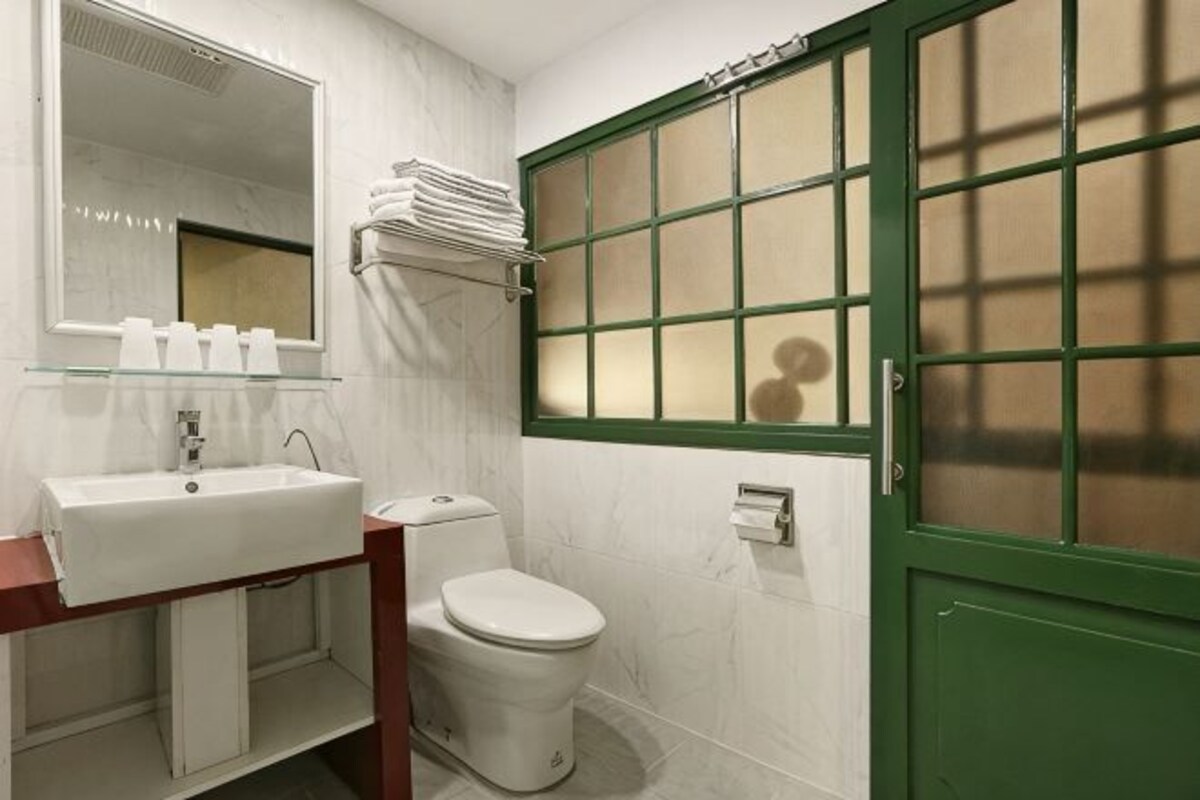 A bathroom with a white sink, mirror, and toilet. There is a window with green frames and a towel rack above the sink.