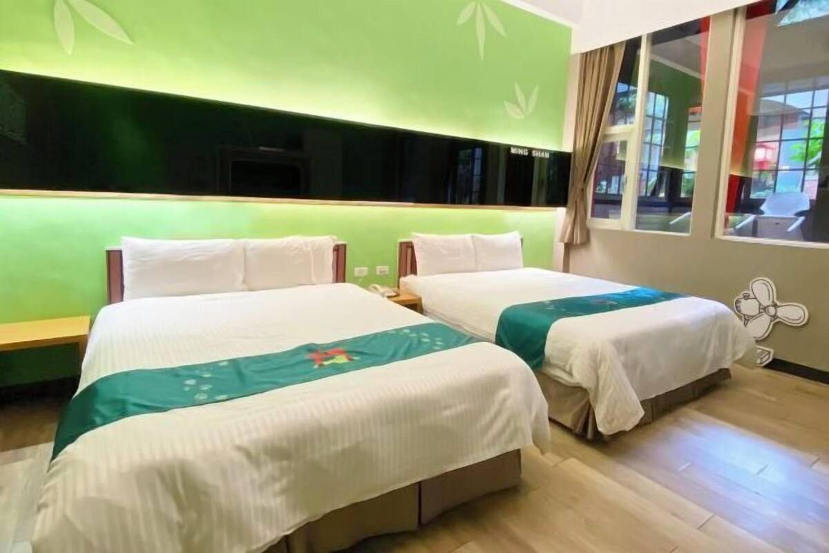 A hotel room with two beds, green walls, and a large window with curtains.