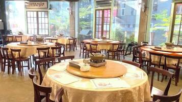Un restaurant avec des tables et des chaises rondes, de grandes fenêtres et une vue sur l’extérieur.