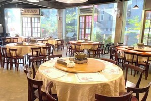 A restaurant with round tables and chairs, large windows, and a view of the outside. - The M Village (Nantou)