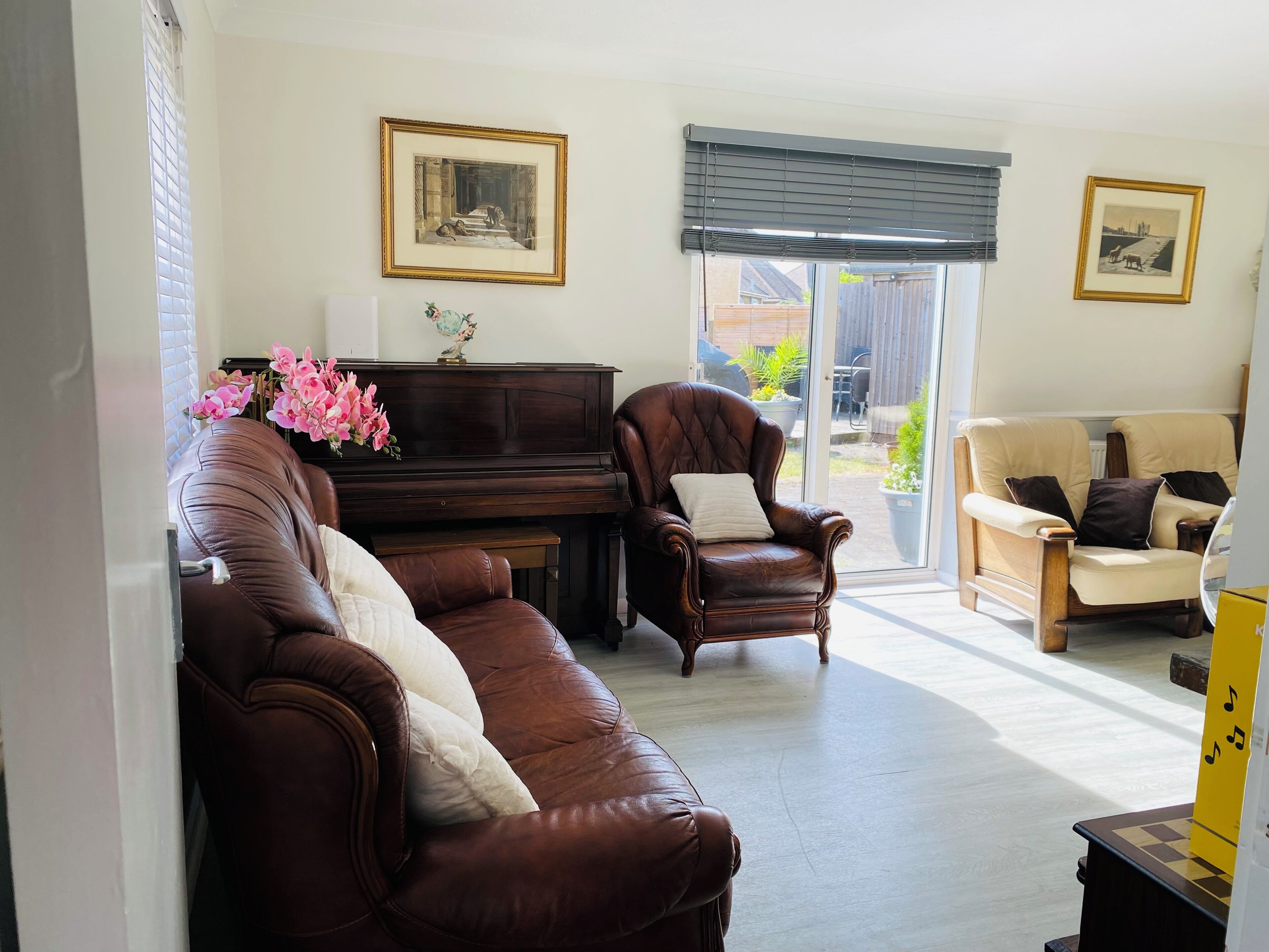 A living room with a dark brown leather sofa, a brown leather armchair, a beige armchair, a piano, and a large window with blinds.